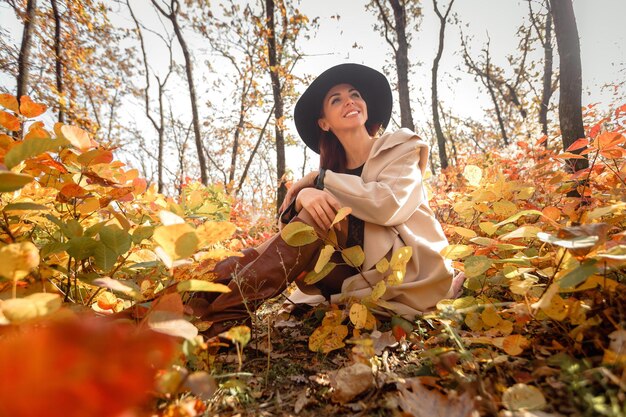 Frau im Kleid und im Hut auf Hintergrund des Herbstlaubs