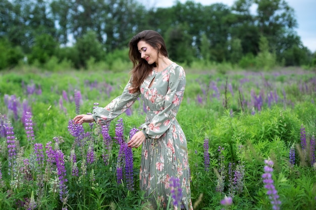 Frau im langen Kleid steht im blühenden Lupinenfeld Mädchen, das auf Sommerfeld mit Wildblumen geht walking