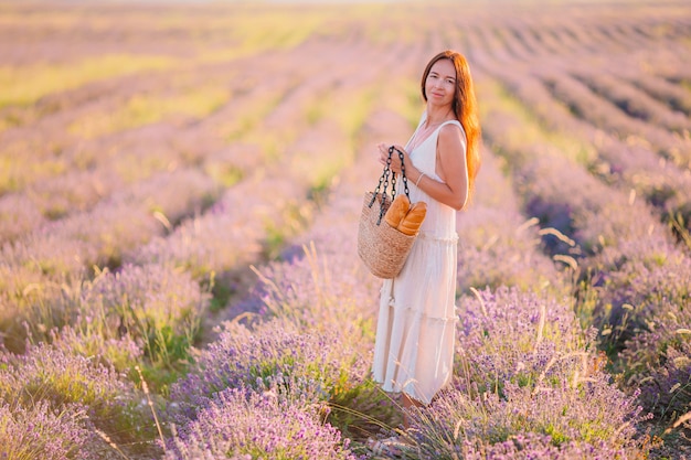 Frau im lavendelblumenfeld bei sonnenuntergang im weißen kleid und im hut