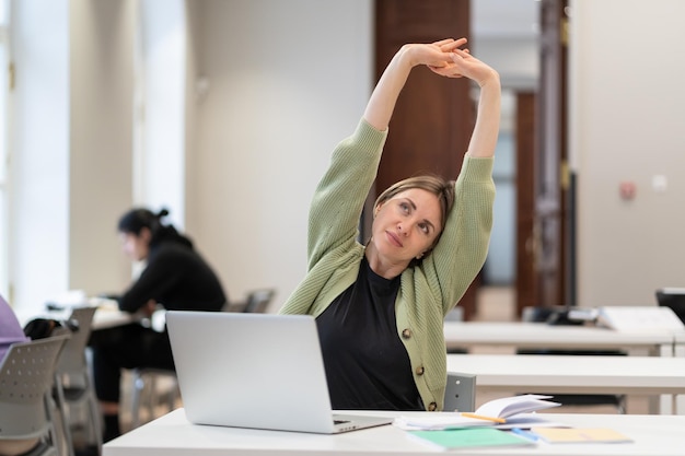 Foto frau im mittleren alter wärmt sich im klassenzimmer mit körper und muskeln auf und fühlt sich mit der geleisteten arbeit zufrieden