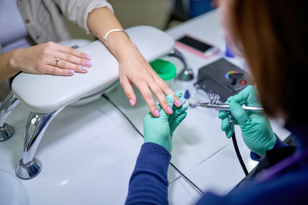 Frau im Nagelstudio, die Gelpoliermaniküre vom Maniküristenmeister empfängt. Sanfte Pflegebehandlung der Nägel