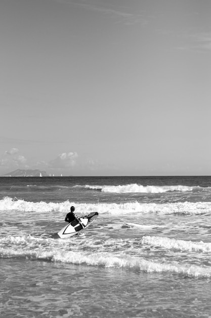 Frau im Neoprenanzug, die mit Surfbrett am Strand ins Meer steigt