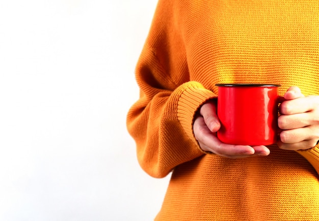 Frau im orangefarbenen Pullover, der rote Tasse auf weißem Hintergrund hält