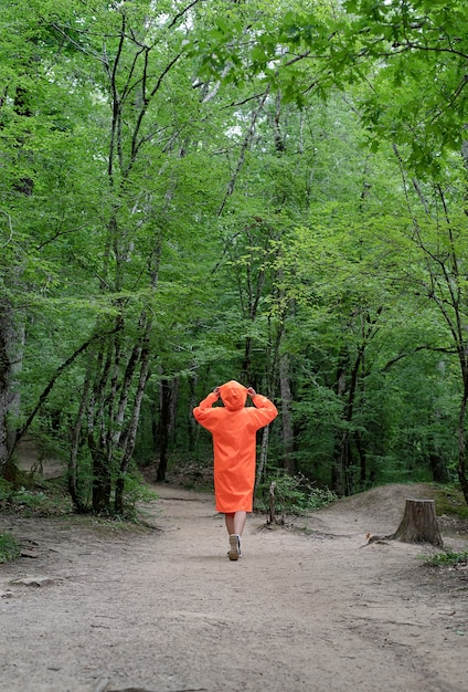 Frau im orangefarbenen Regenmantel, die im Wald spaziert