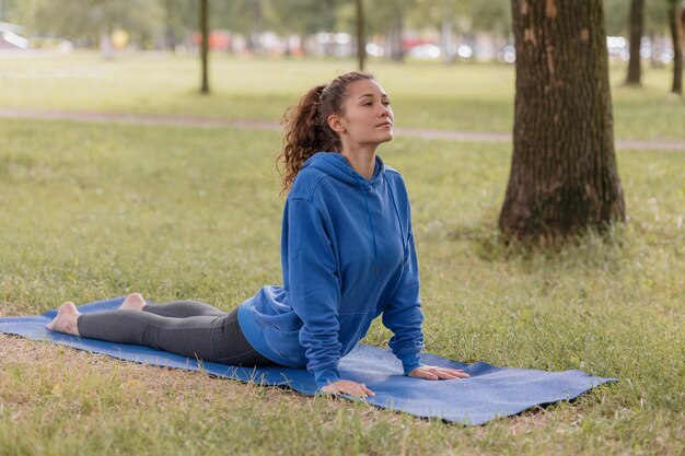 Frau im Park macht Yoga-Sportmeditation oder Fitness auf einer Yogamatte eine europäische Frau mit Locken