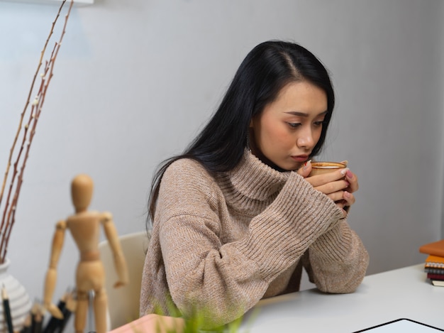 Frau im Pullover hält eine Tasse heißen Lattekaffee