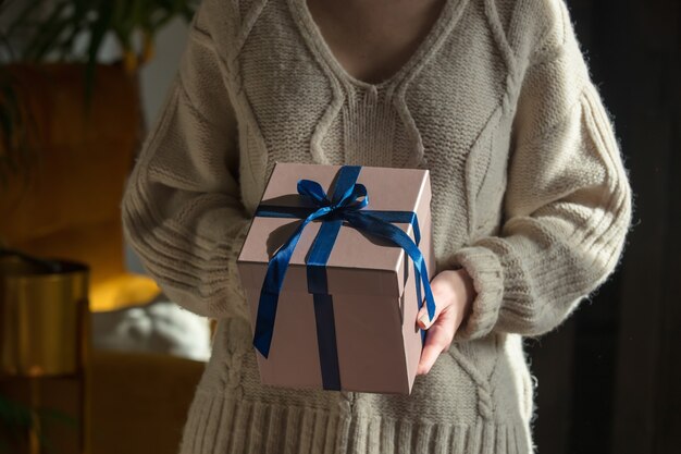 Frau im Pullover hält Geschenkbox zu Hause