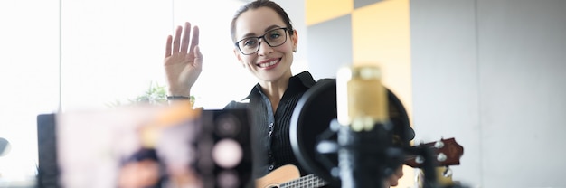 Foto frau im rollstuhl hält ukulele und winkt der kamera freiberuflich für menschen mit