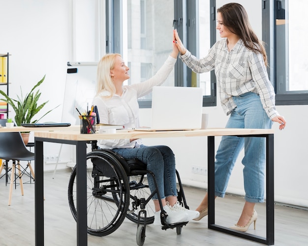 Frau im Rollstuhl hoch fünffach ihre Mitarbeiterin im Büro