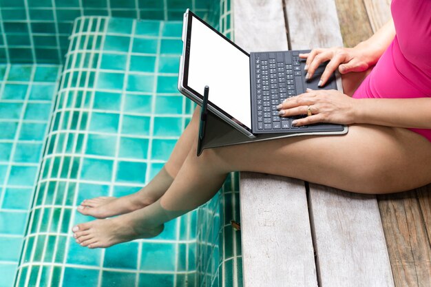 Frau im rosa Badeanzug, der am Laptop durch den Pool arbeitet.