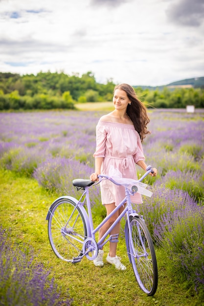 Frau im rosafarbenen Kleid mit Retro-Fahrrad im Lavendelfeld Tschechien