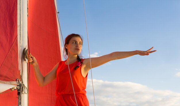Frau im roten kleid mit ängstlichem gesichtsausdruck, die auf einem segelboot steht, zeigt die hand nach vorne