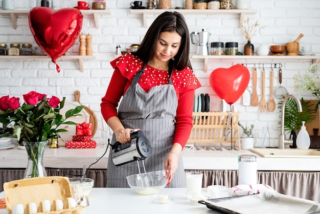 Frau im roten Kleid und in der grauen Schürze, die Valentinskekse an der Küche machen
