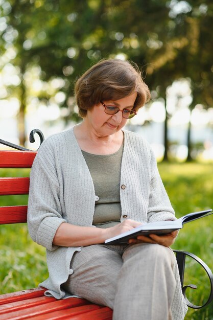 Frau im Ruhestand, die ein Buch auf der Bank liest