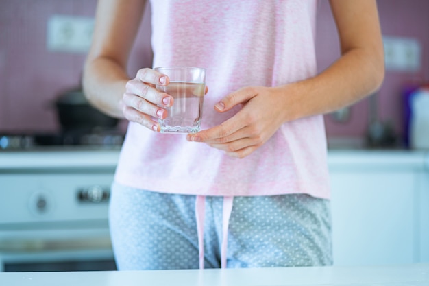 Frau im Schlafanzug hält ein Glas klares gereinigtes Wasser in den Händen am Morgen in der Küche zu Hause