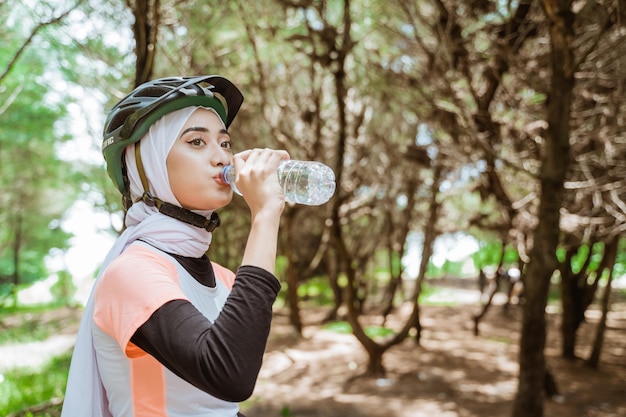 Frau im Schleier trinkt Mineralwasser in Flaschen während der Fahrradpause