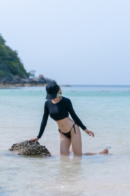 Frau im schwarzen Bikini am tropischen Strand. Porträtfrau in Badebekleidung, die am Strand im Wasser genießt und sitzt.