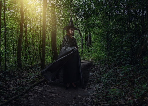 Frau im schwarzen furchtsamen Hexenhalloween-Kostüm mit Mondschein in einem dunklen Wald