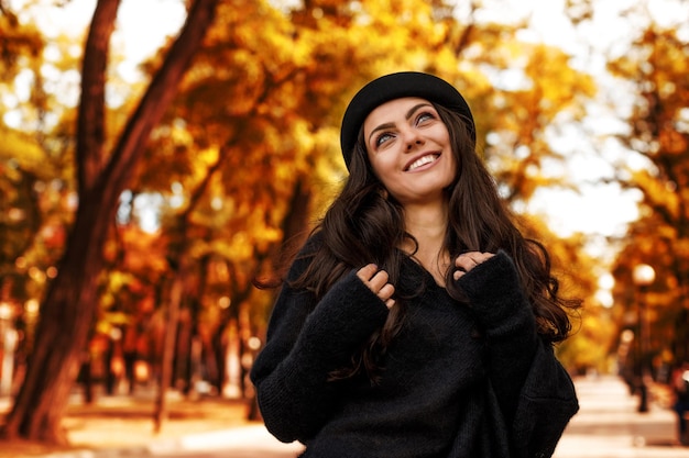 Frau im schwarzen Hut auf dem Hintergrund der Herbstblätter