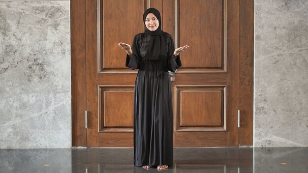 Frau im schwarzen muslimischen Kleid signalisiert Willkommen an der Tür