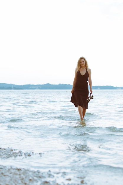 Frau im Schwarzlichtkleid, die barfuß am Meeresstrand spazieren geht