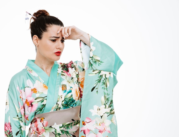 Frau im traditionellen japanischen Kimono, der verwirrt die Hand auf ihrem Kopf auf Weiß hält