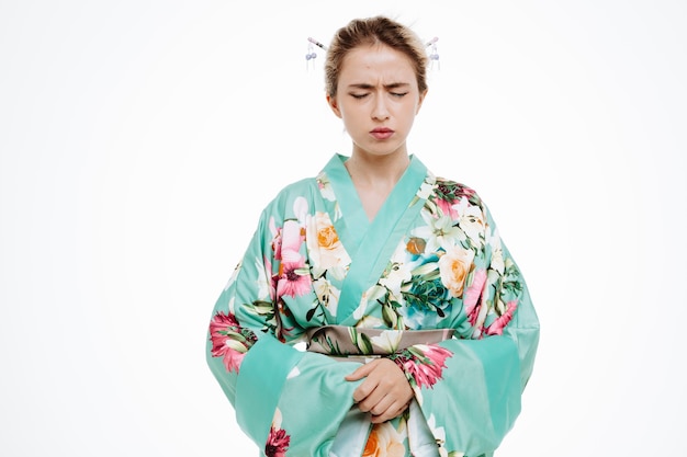 Foto frau im traditionellen japanischen kimono, die unwohl aussieht und ihren bauch berührt, der unter schmerzen auf weiß leidet