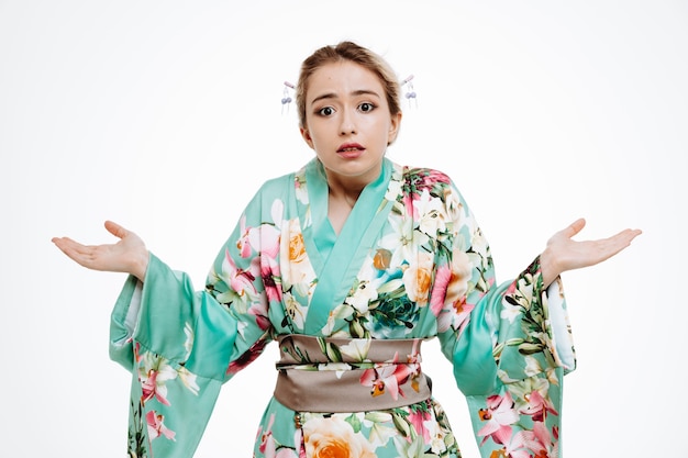 Frau im traditionellen japanischen Kimono verwirrt, die Arme zu den Seiten ausbreitend, die Zweifel an Weiß haben