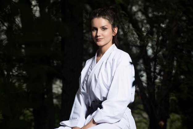 Frau im traditionellen Kimono, die sich ausruht, nachdem sie ihre Karate-Bewegungen in einem bewaldeten Waldgebiet geübt hat