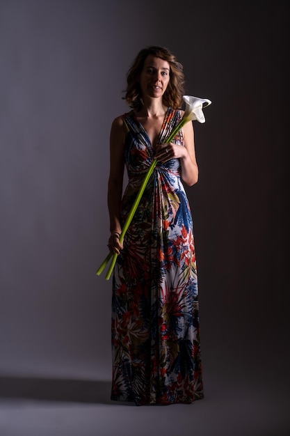 Frau im Vintage-Blumenkleid mit einer Blume in der Hand auf schwarzem Hintergrund