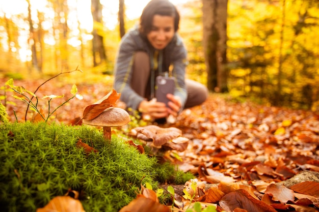 Frau im Wald fotografiert mit Smartphone einen Pilz