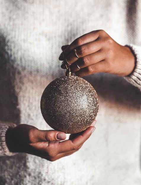 Frau im warmen Pullover, der dekorativen Glasball des Spielzeugs in den Händen hält, Kopienraum. Weihnachten, Feiertagsfeierkonzept des neuen Jahres