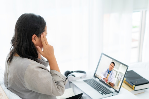 Frau im weißen Bett, die mit dem Arzt spricht, der Telegesundheitstechnologie verwendet