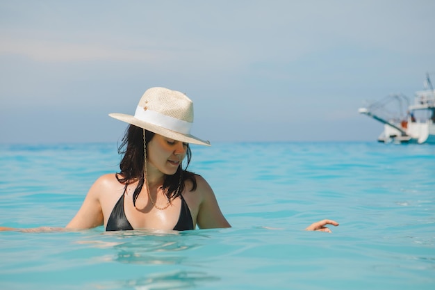 Frau im weißen Hut und im schwarzen Badeanzug in den Sommerferien des blauen Meerwassers