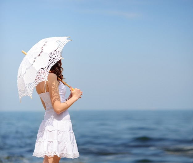 Frau im weißen Kleid auf einem Meeresstrand, der sich mit Sonnenschirm vor der Sonne versteckt, kein Gesicht