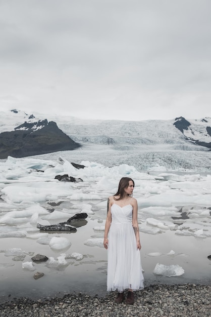 Frau im weißen Kleid steht vor dem Hintergrund der Gletscher in Island