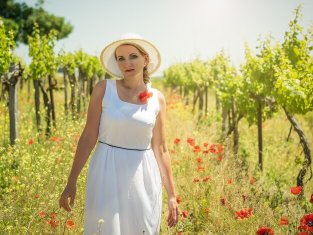 Frau im weißen Kleid und Hut in den Reihen der Traubenfelder.