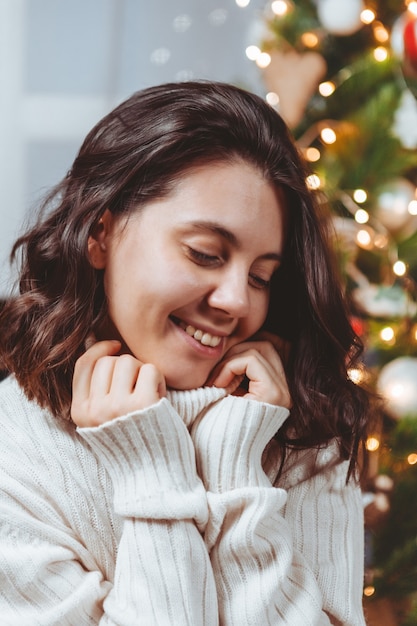 Frau im weißen Pullover posiert in der Nähe von Weihnachtsbaumporträt