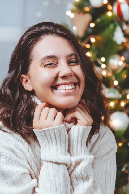 Frau im weißen Pullover posiert in der Nähe von Weihnachtsbaumporträt