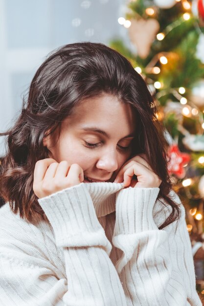 Frau im weißen Pullover posiert in der Nähe von Weihnachtsbaumporträt