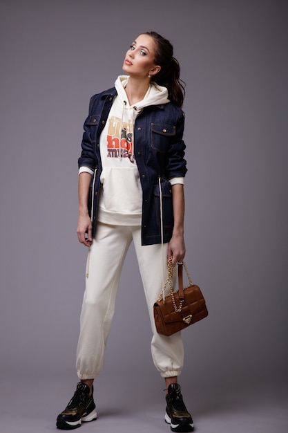 Frau im weißen Sportanzug mit Kapuze Denim Jeansjacke Sneakers Walking Style Handtasche