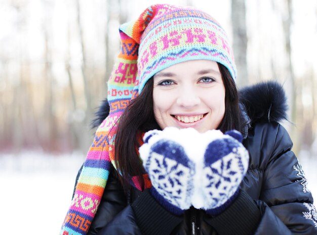 Frau im Winterpark weht spielerisch Schnee