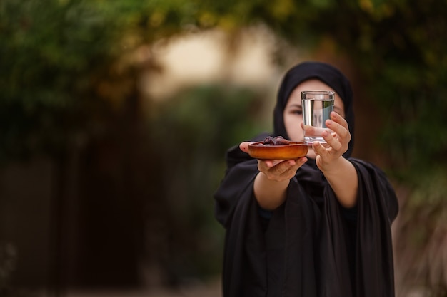 Frau in Abaya hält eine Dattelfrucht und ein Glas Wasser aus ihrer Ramadan-Feier