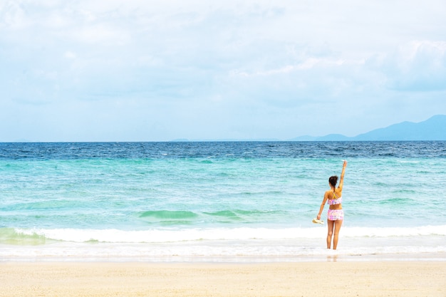 Frau in anhebender Hand des Bikinis und in schauender Ansicht des tropischen Strandes