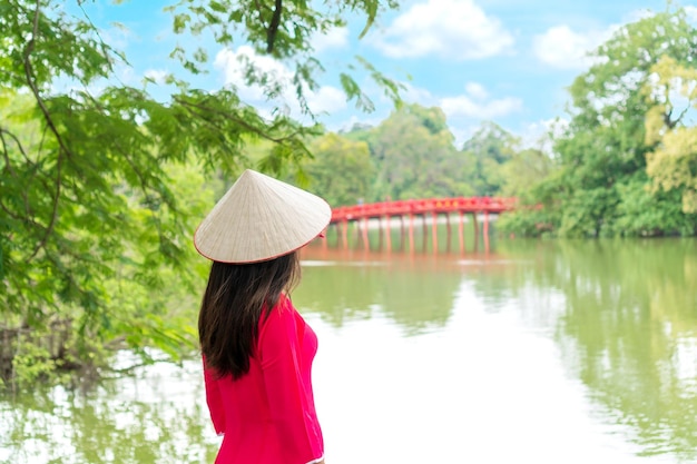 Frau in Ao Dai Stand am See Blick auf die Rote Brücke in Hoan Kiem Lake Hanoi Vietnam