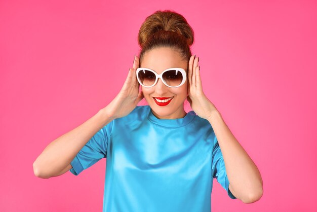 Frau in blauem Seidenkleid und weißer Sonnenbrille auf rosafarbenem Hintergrund