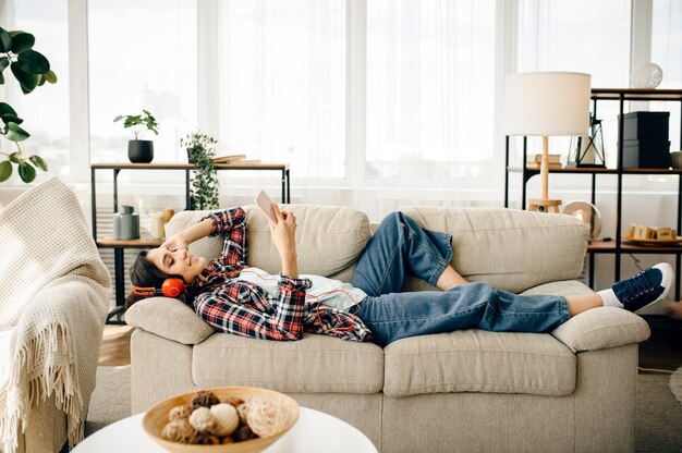 Frau in den Kopfhörern, die Musik auf Sofa hören.