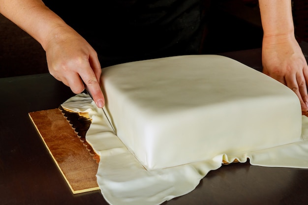 Frau in der Bäckerei, die weißen Fondant der Hochzeitstorte bedeckt