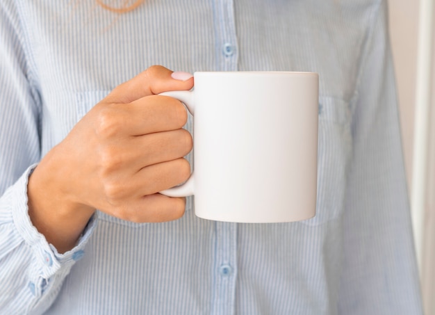 Frau in der Bluse, die eine warme Tasse Kaffee hält