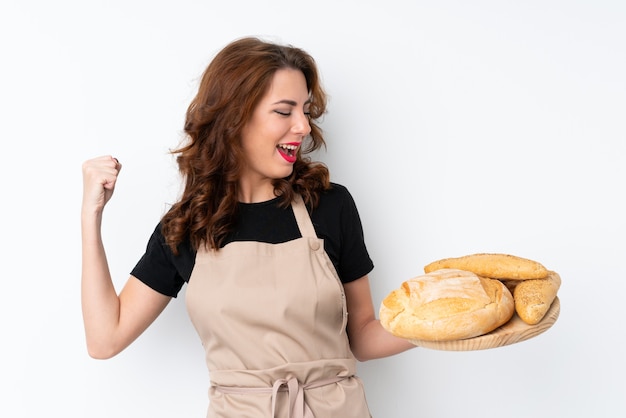 Frau in der Chefuniform. Weiblicher Bäcker, der eine Tabelle mit einigen Broten feiern einen Sieg hält